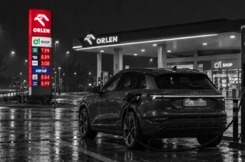 Audi Q6 e-tron przy ładowarce ORLEN Charge obok pylonu z cenami paliw
